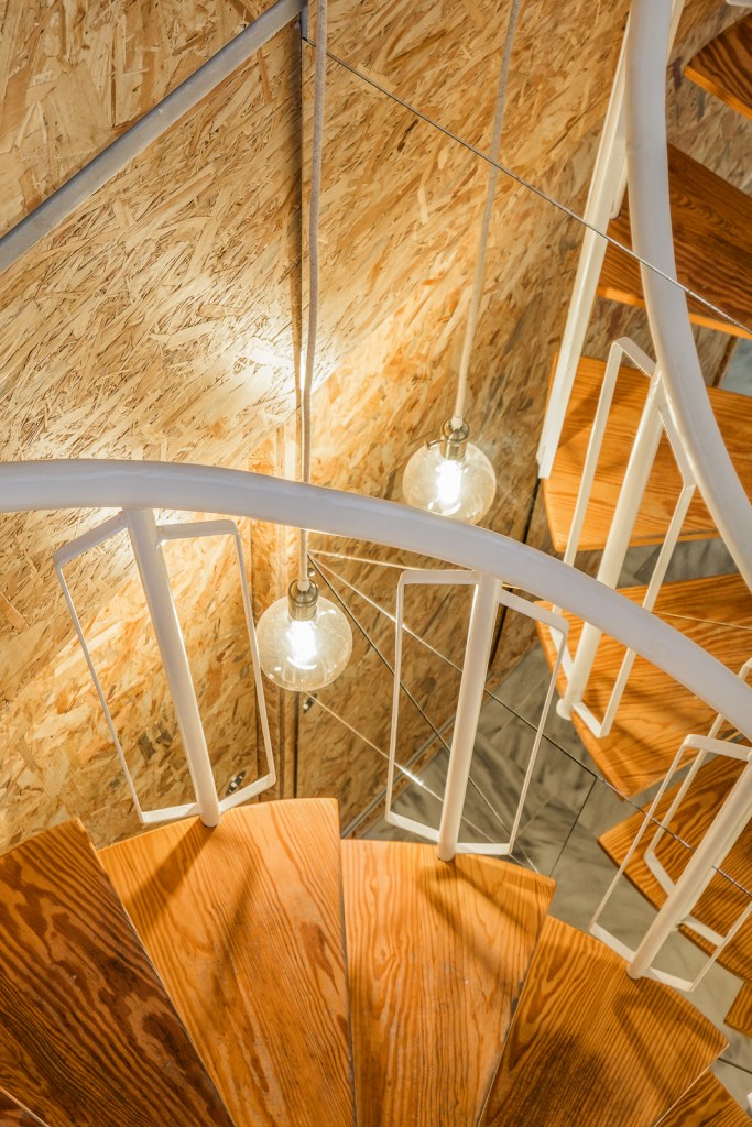 Vista superior de la escalera de caracol restaurada, con peldaños de madera, estructura metálica y revestimientos de tablero OSB en Casa Atelier.